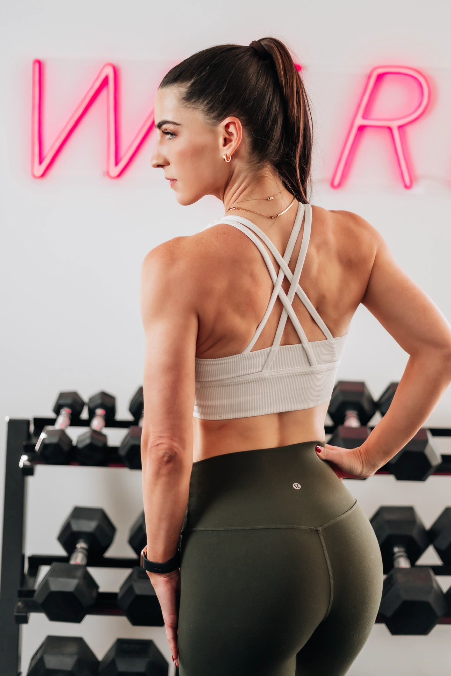 Katie in a gym, standing in front of a rack of dumbbells